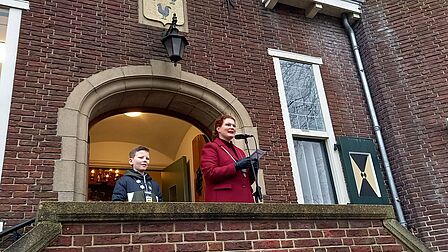 Burgemeester Magda Jansen staat samen met kinderburgemeester Fedde op het bordes voor het gemeentehuis en geeft haar toespraak.